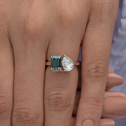 Ring close-up on hand with emerald-cut green center and pear-cut clear accent