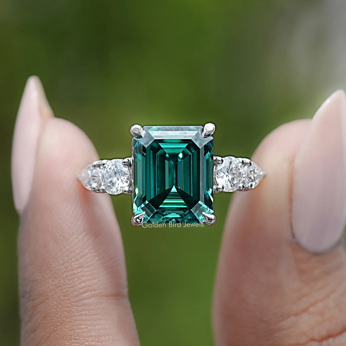 Silver five-stone ring featuring emerald-cut green center stone with four side stones