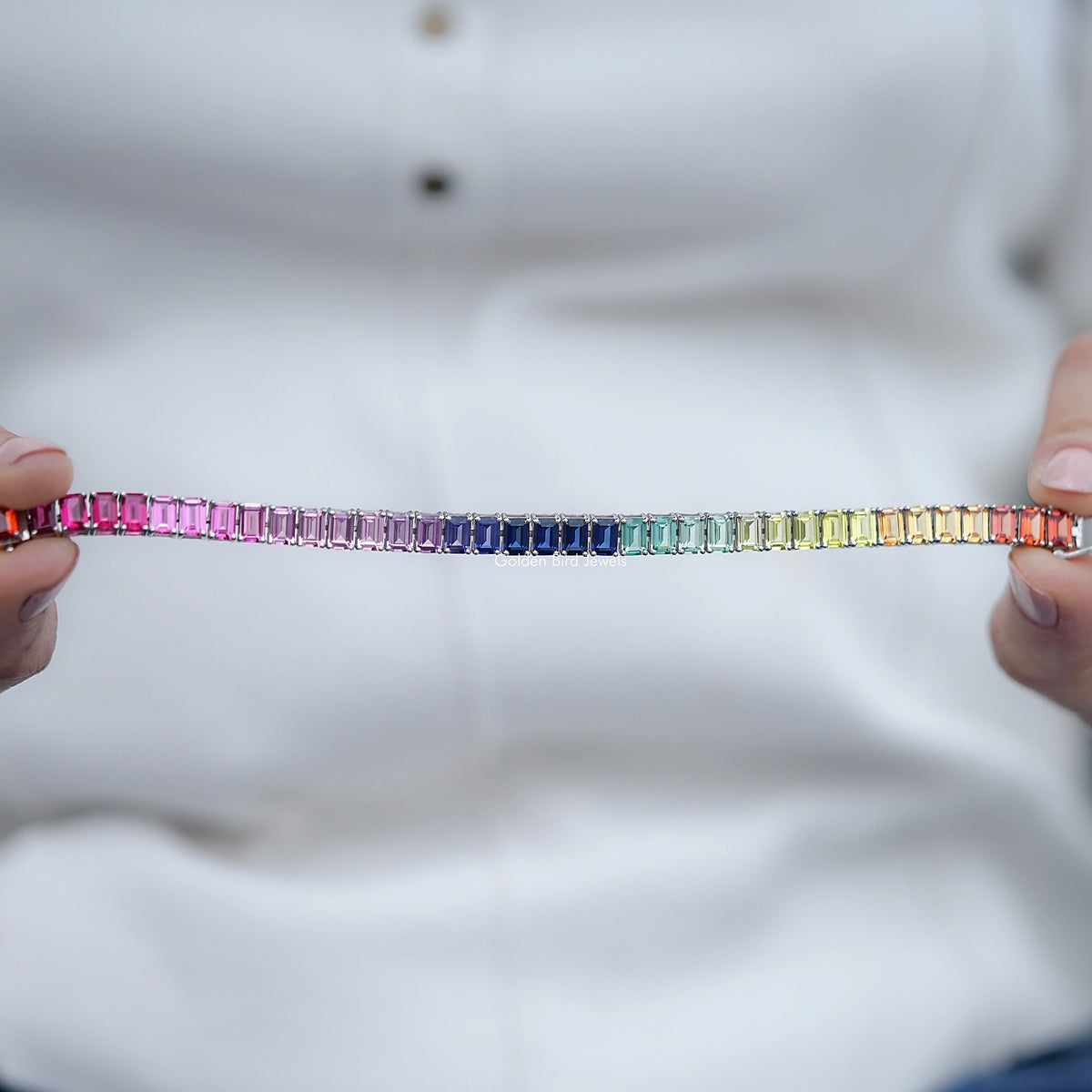 Multi-color tennis bracelet with rainbow rows of rectangular gemstones, held by hands