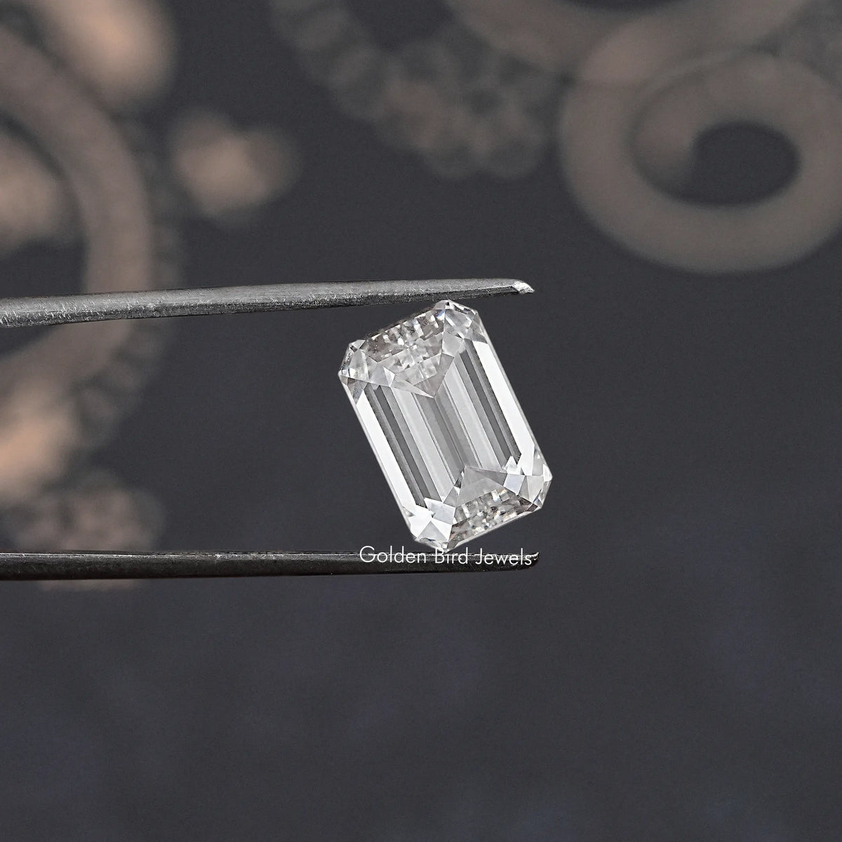 Loose emerald-cut lab-grown diamond held between tweezers, showing table and facets