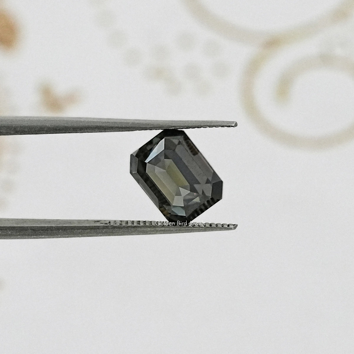 Emerald-cut dark gray moissanite gemstone between metal tweezers