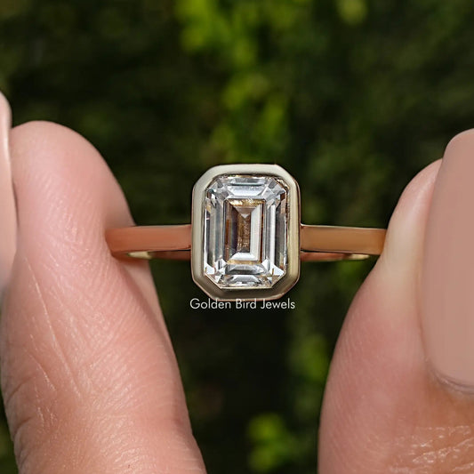 Solitaire moissanite ring with emerald-cut stone in bezel set, gold-tone band