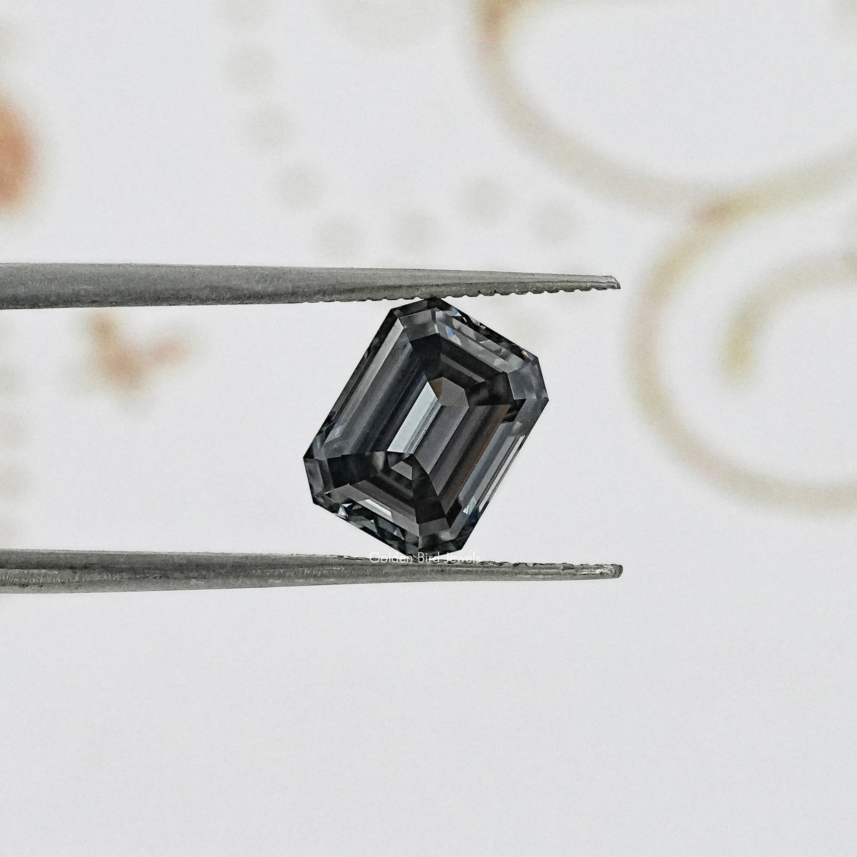 Gray emerald-cut gemstone held in tweezers, side-on view with facets