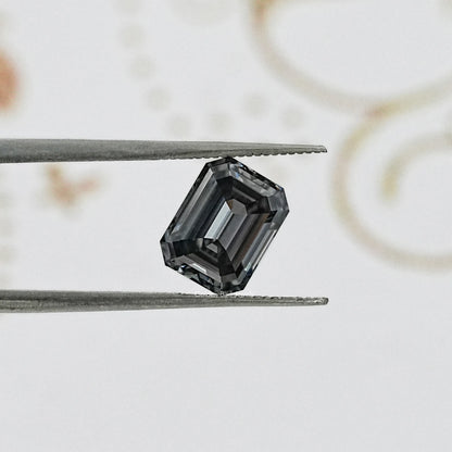 Gray emerald-cut gemstone held in tweezers, side-on view with facets