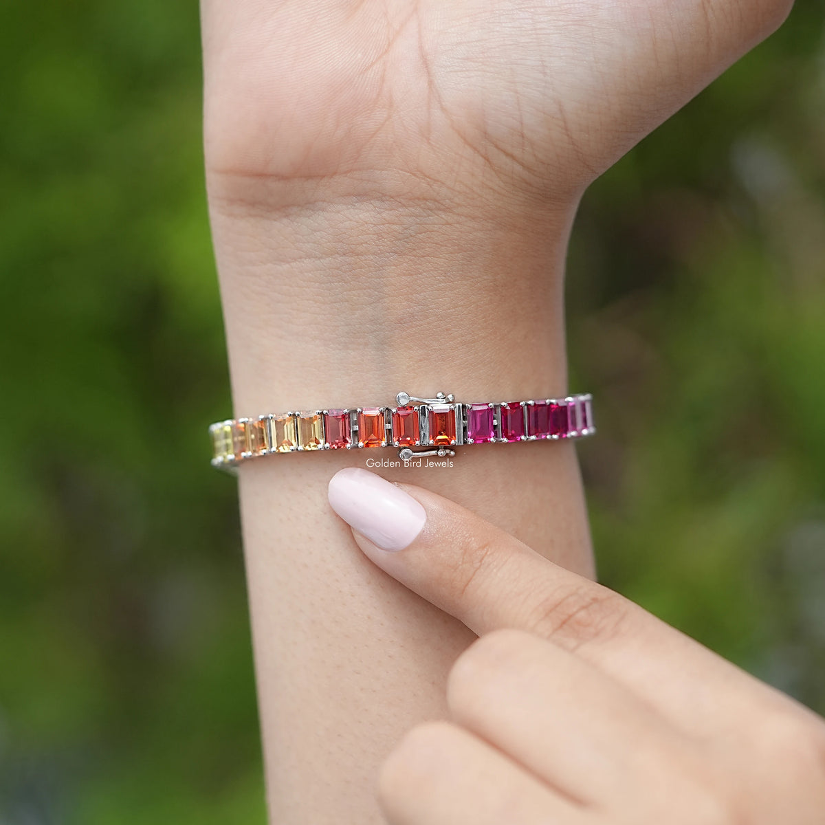 Rainbow multi-color gemstone tennis bracelet on wrist with orange, pink, blue and green stones