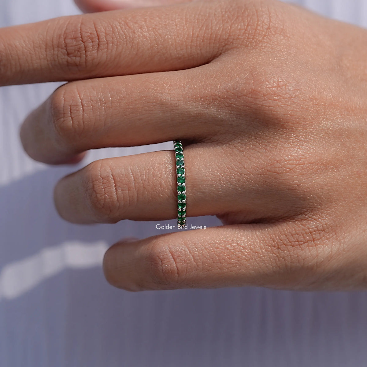 Emerald green eternity band ring on finger, side view of round stones