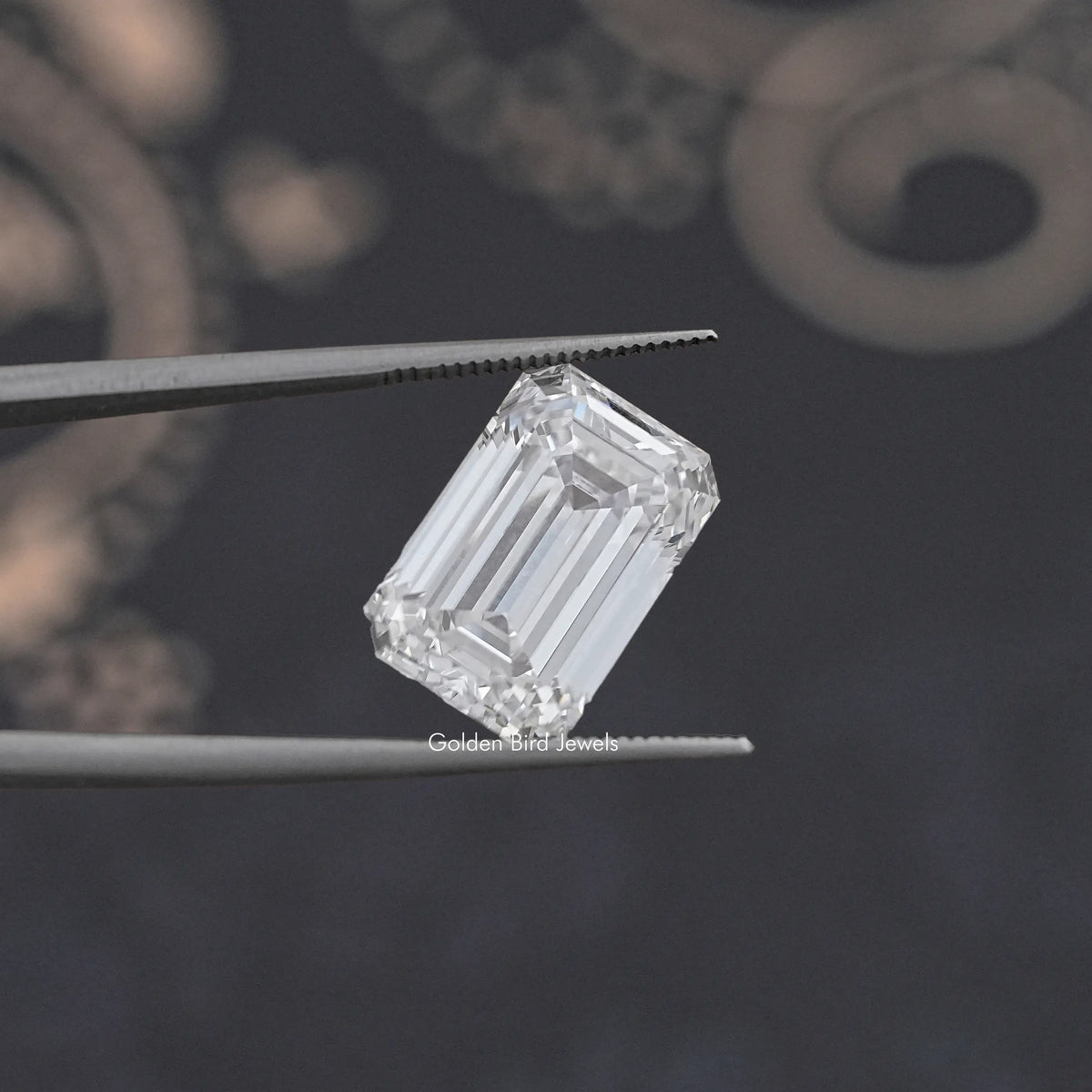 Emerald-cut loose lab diamond, clear, held between metal tweezers.