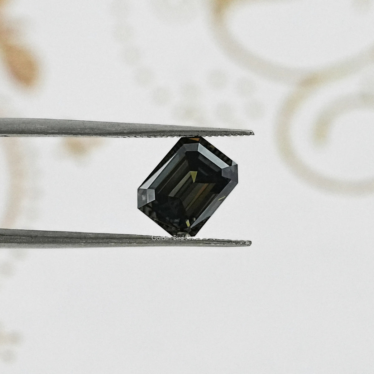 Emerald-cut dark gray moissanite gemstone held between metal tweezers