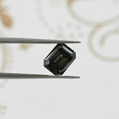 Emerald-cut dark gray moissanite gemstone held between metal tweezers