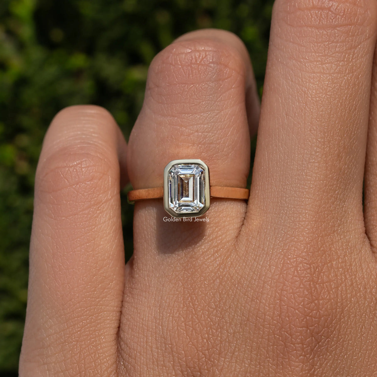 Emerald-cut moissanite solitaire ring with bezel-set center stone, gold-tone band