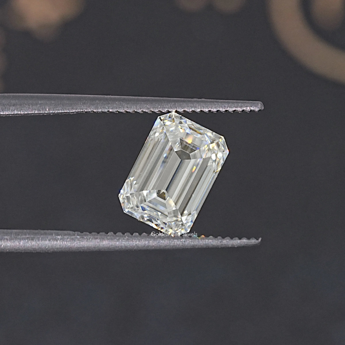 Near colorless emerald-cut moissanite loose stone held by tweezers, angled view