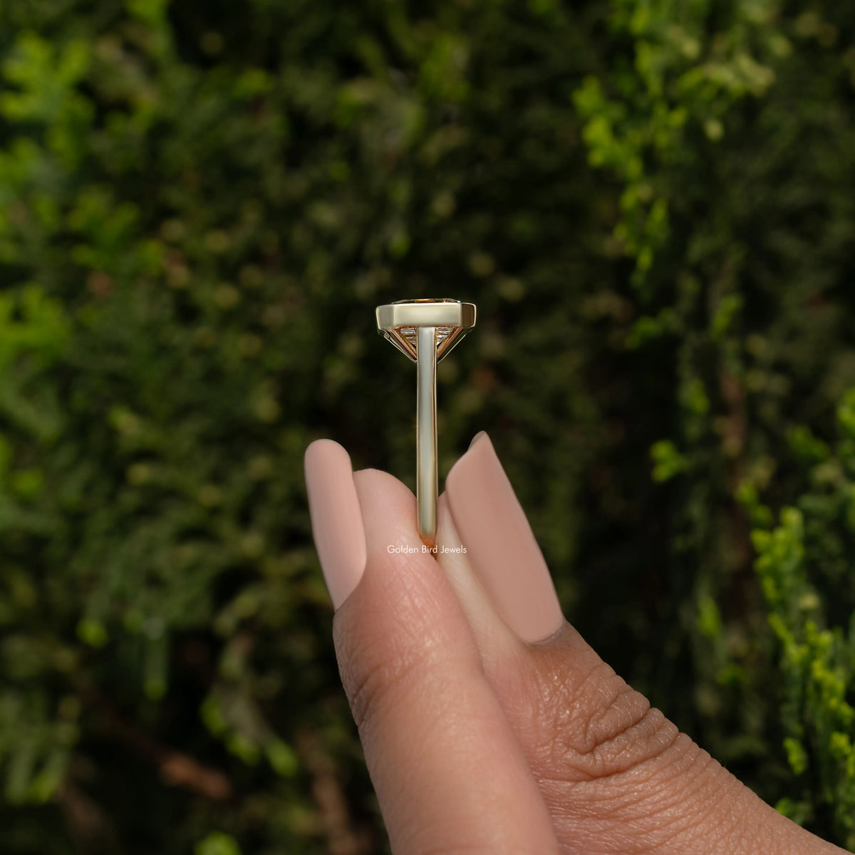 Emerald-cut bezel-set solitaire moissanite ring on slim gold-tone band, side view