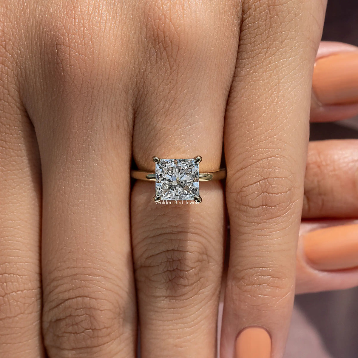 Princess-cut diamond solitaire ring on finger, detailed view of prongs