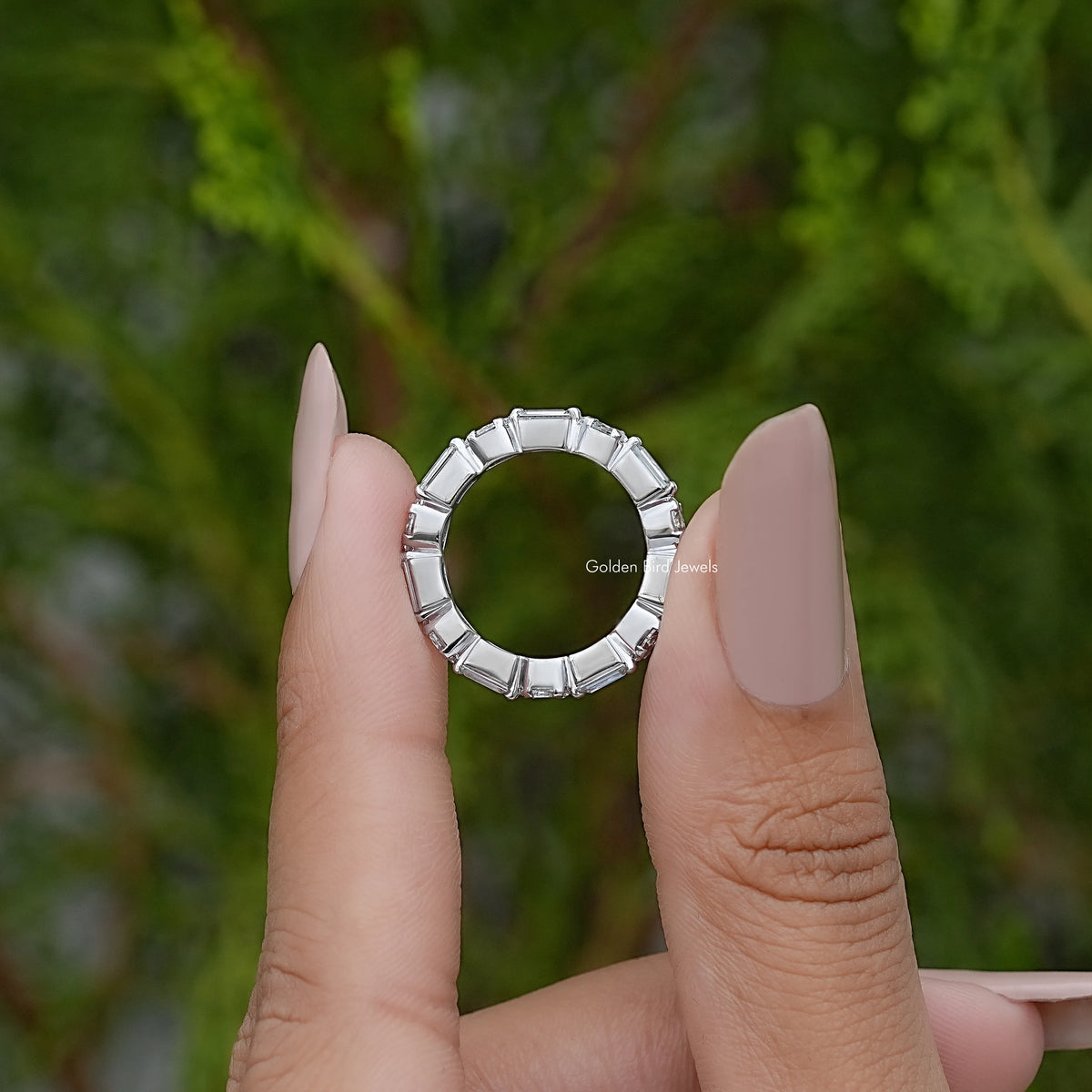 Silver eternity wedding band with marquise stones, top view held between fingers