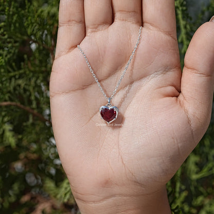 Heart solitaire necklace with red gemstone on silver chain, close-up in palm