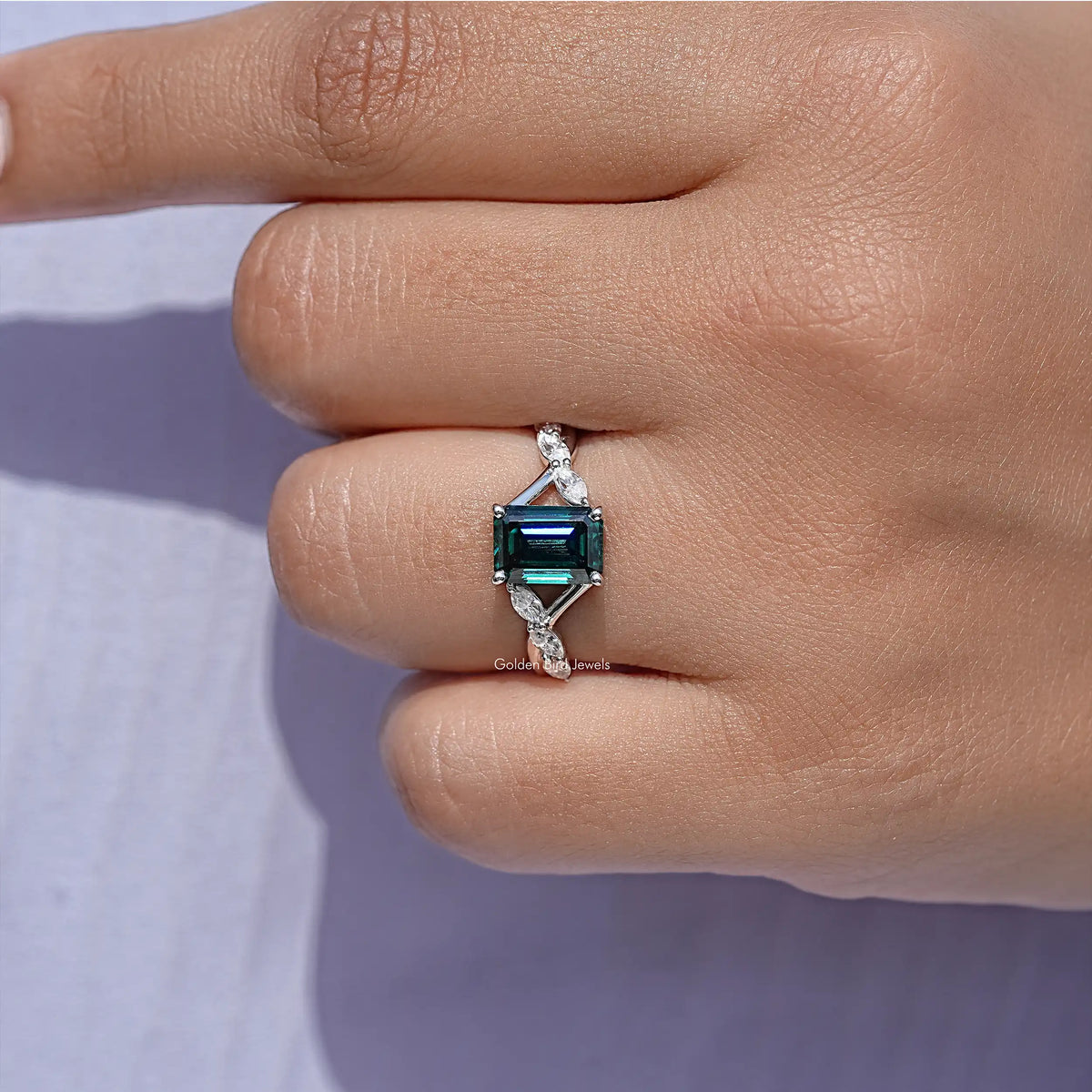 Sterling silver green emerald-cut moissanite ring on finger with floral side details.