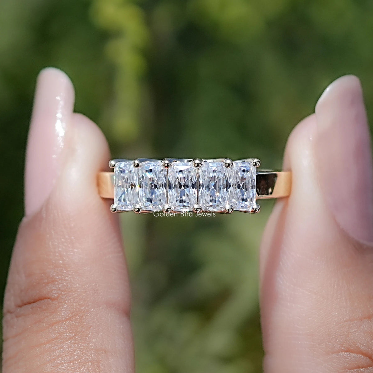 Five radiant-cut moissanite stones in a band ring, close-up front view on fingers