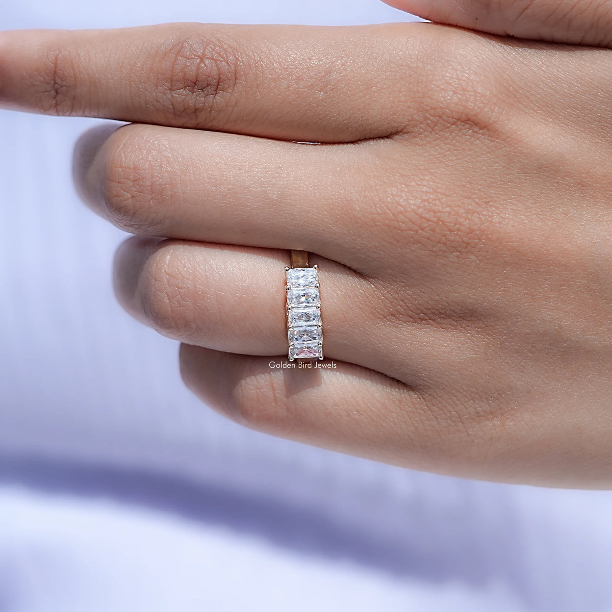 Five-stone moissanite radiant-cut band ring on finger, straight view of top profile