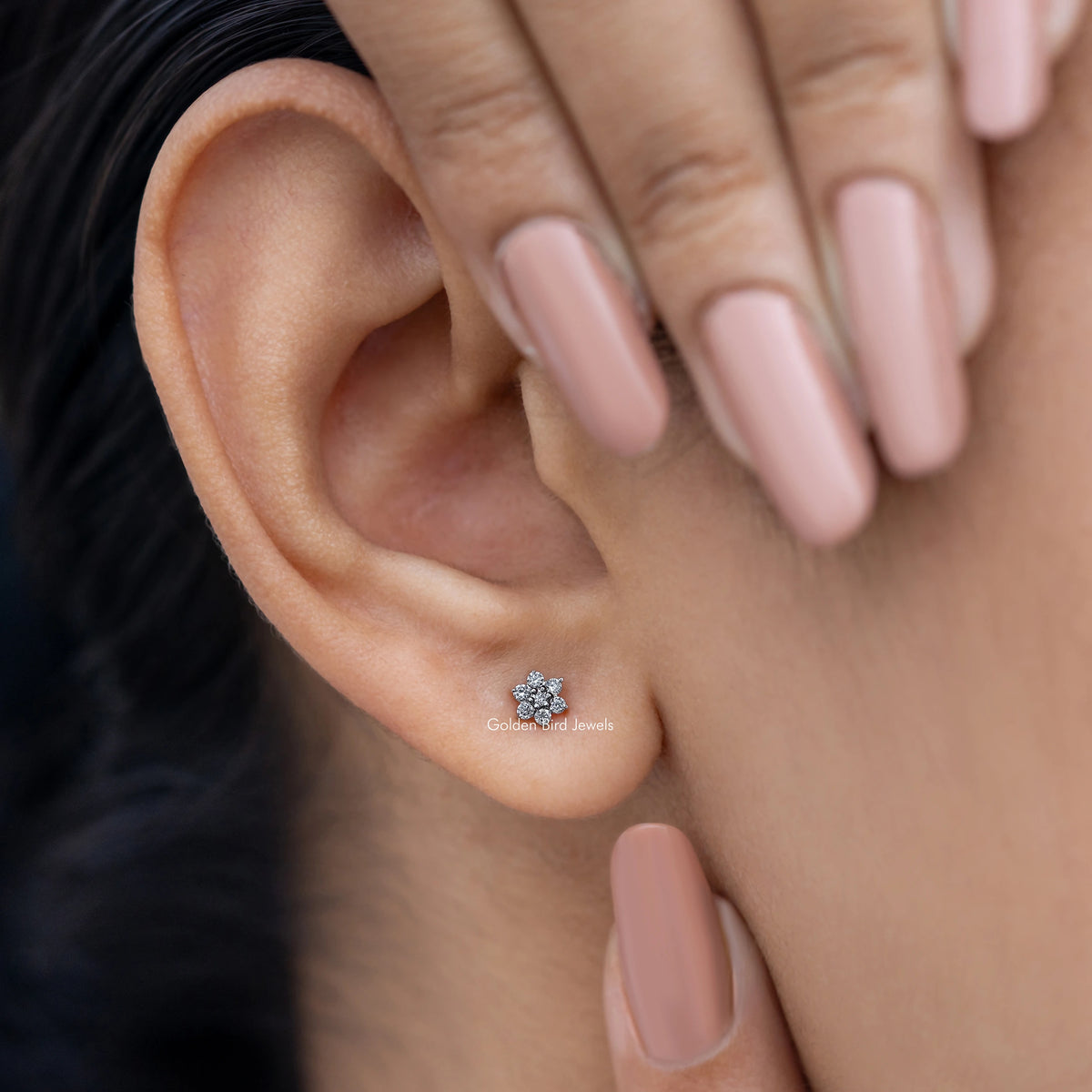 Small floral diamond stud earring on ear, subtle round flower-like stone cluster.