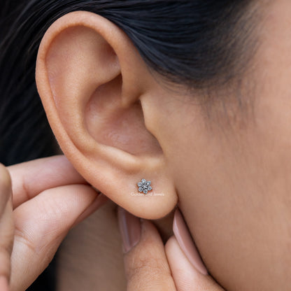 Floral diamond stud earring near ear, small round flower-like stone cluster on post.