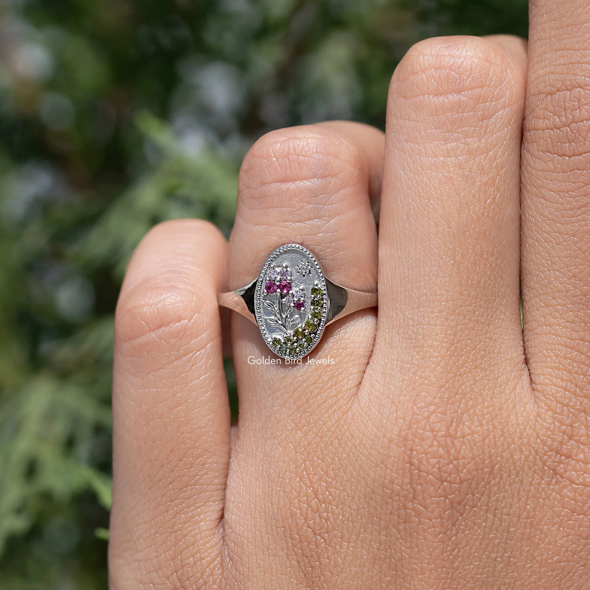 Floral oval signet ring on finger, silver-tone setting with pink and greenish stones