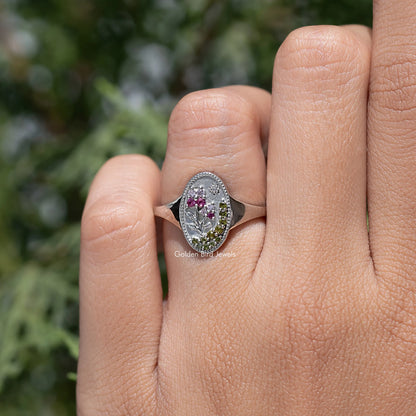 Floral oval signet ring on finger, silver-tone setting with pink and greenish stones