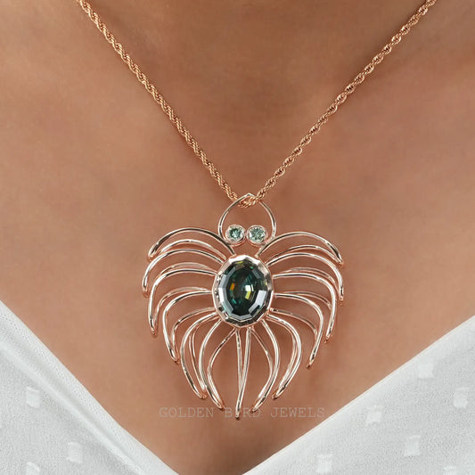 Rose gold oval moissanite spider pendant with green center stone and web-like prongs