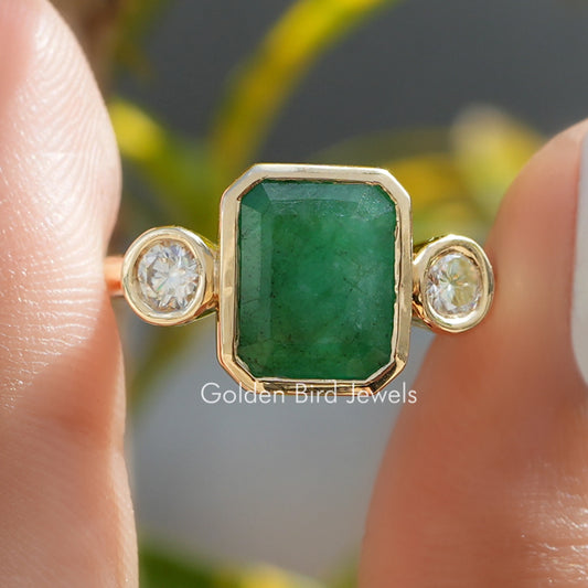 Gold-tone three-stone ring with emerald green bezel centerpiece and two round side stones