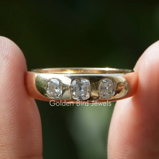 Old mine cushion-cut three-stone moissanite ring with three clear stones on a gold-tone band