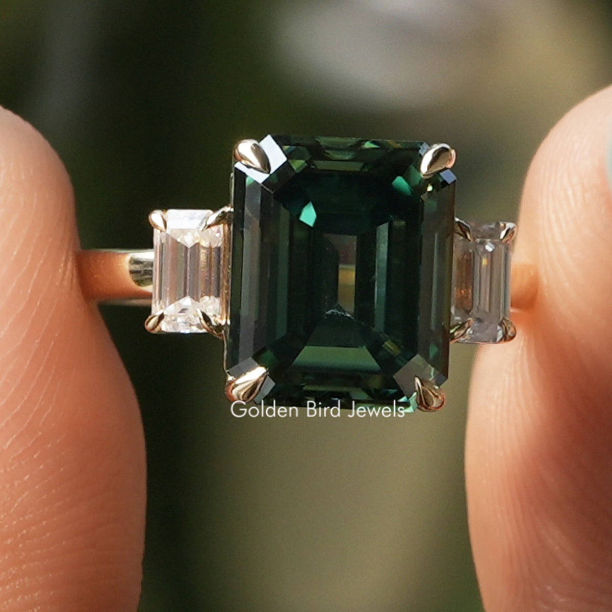 Three-stone ring with emerald-cut dark green center stone and clear side stones, silver band