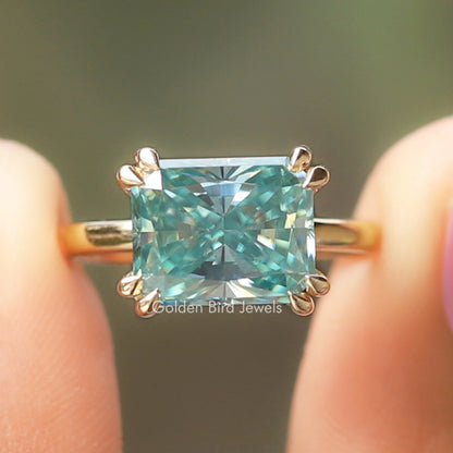 Emerald-cut teal moissanite engagement ring with 4-prong setting and side scroll details