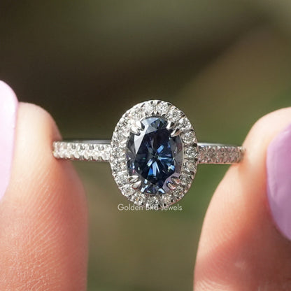 Oval blue sapphire halo engagement ring with round white stones on slim band
