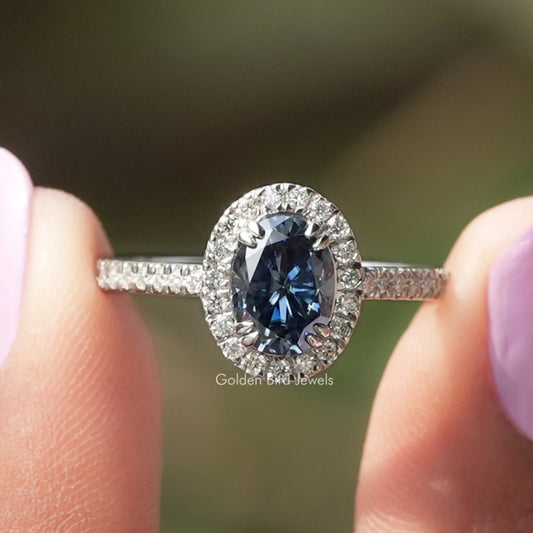 Oval blue sapphire halo engagement ring with round white stones on slim band