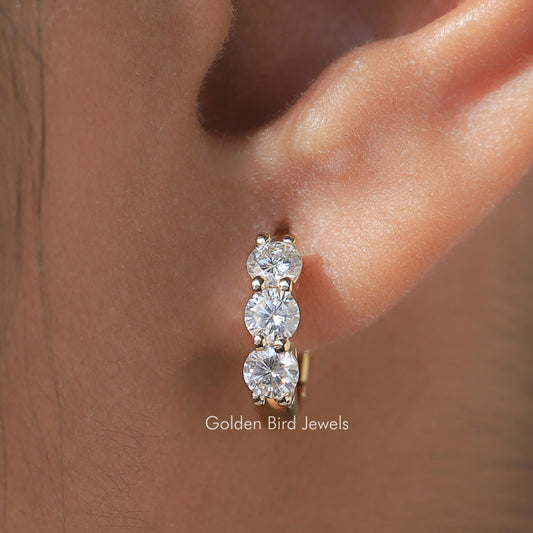 Gold-tone huggie hoop earrings with three round-cut stones, close-up on ear