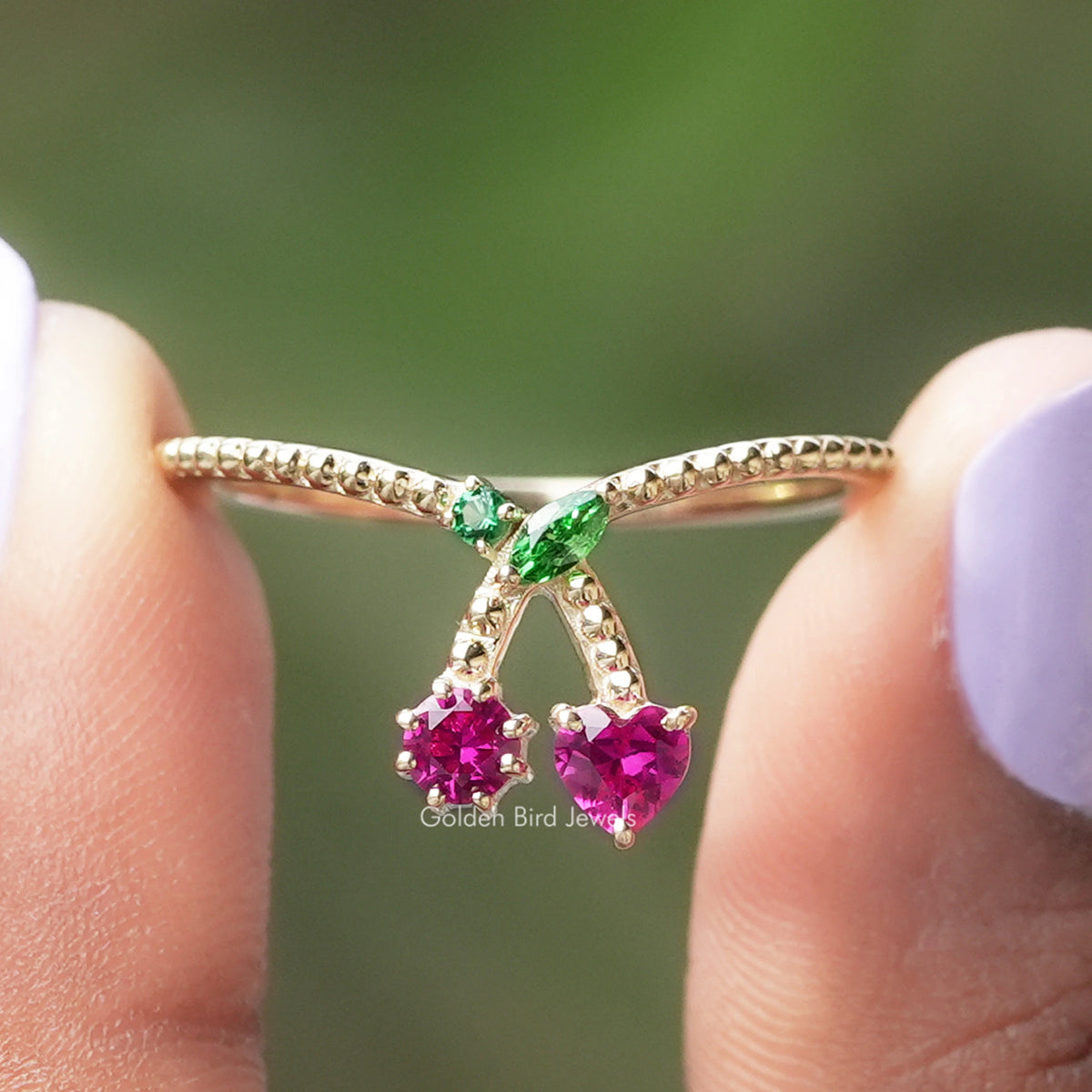 Gold-tone ring with three dangling heart-shaped pink gemstones and small green center