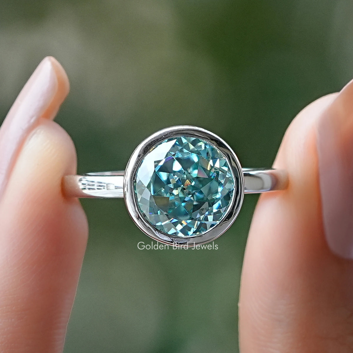 Bezel-set round moissanite ring with teal stone on polished silver band