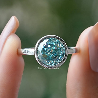 Bezel-set round moissanite ring with teal stone on polished silver band