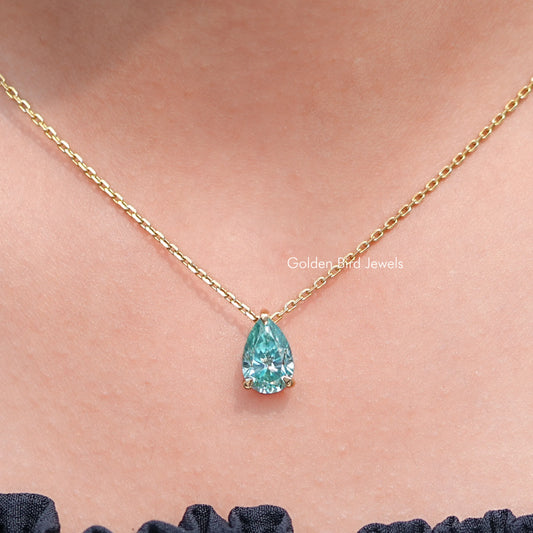 Pear-cut teal teardrop gemstone pendant on gold chain, close-up.