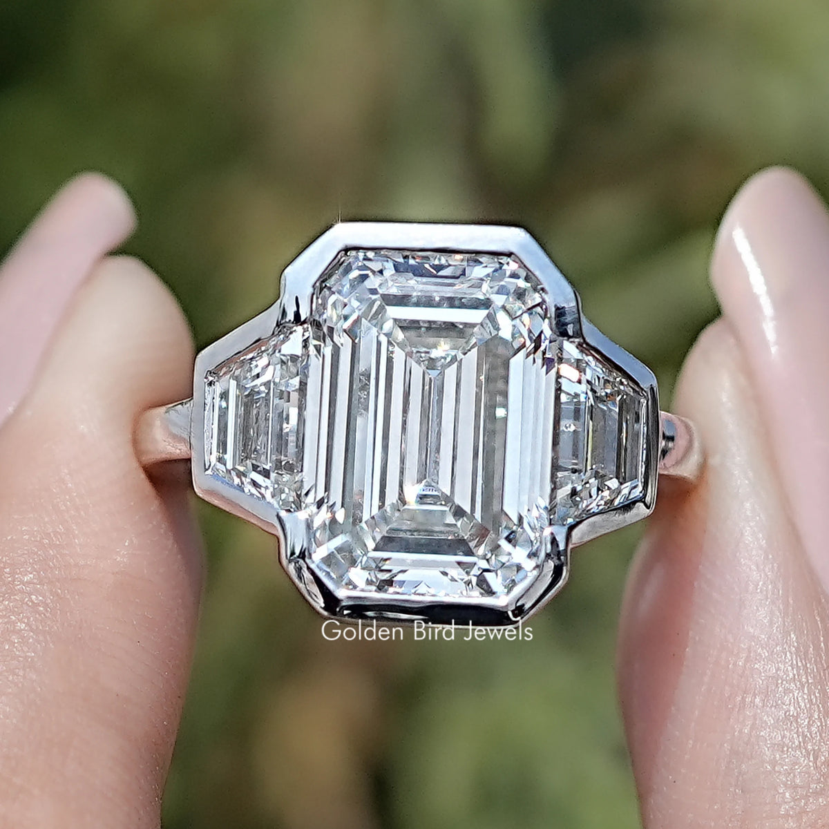 Front view of Bezel Set Emerald Cut Lab Diamond Three Stone Ring in two fingers 