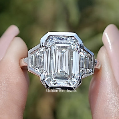 Front view of Bezel Set Emerald Cut Lab Diamond Three Stone Ring in two fingers 