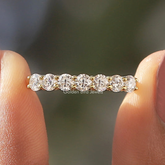 Gold-tone round-cut eternity band with seven clear stones, held between fingers