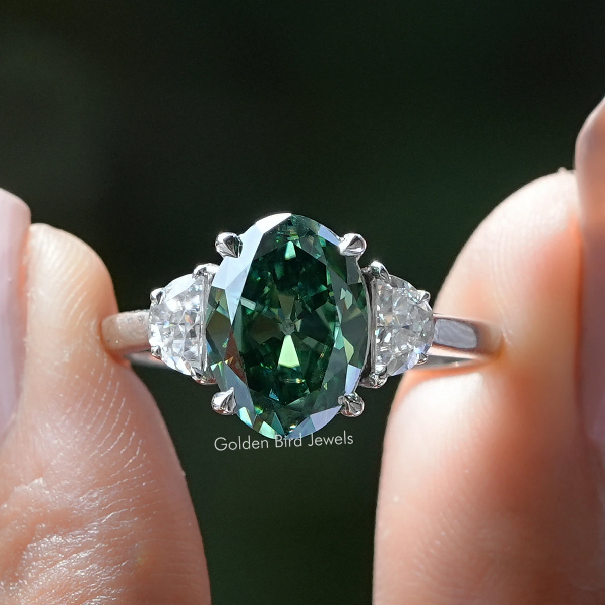 Three-stone oval ring with dark green center stone and clear side stones, sterling silver band
