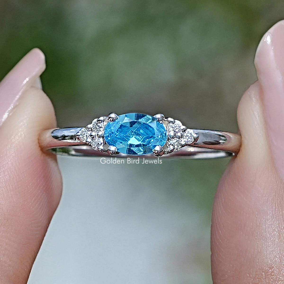 Silver ring with oval blue gemstone and small side stones around a halo setting