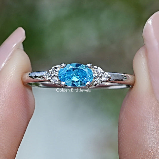Silver ring with oval blue gemstone and small side stones around a halo setting