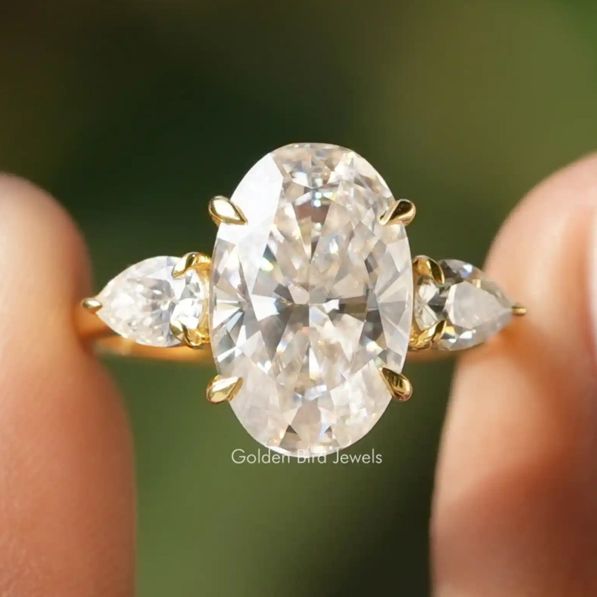 Three-stone moissanite ring with oval center stone and pear side stones, gold-toned prongs.