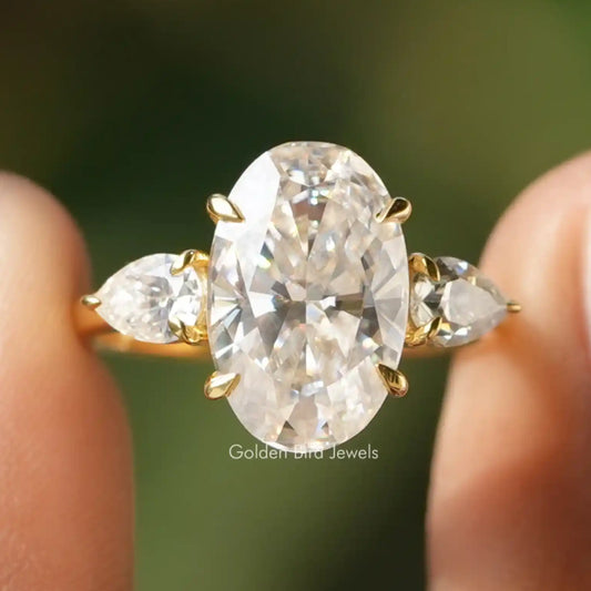 Three-stone moissanite ring with oval center stone and pear side stones, gold-toned prongs.