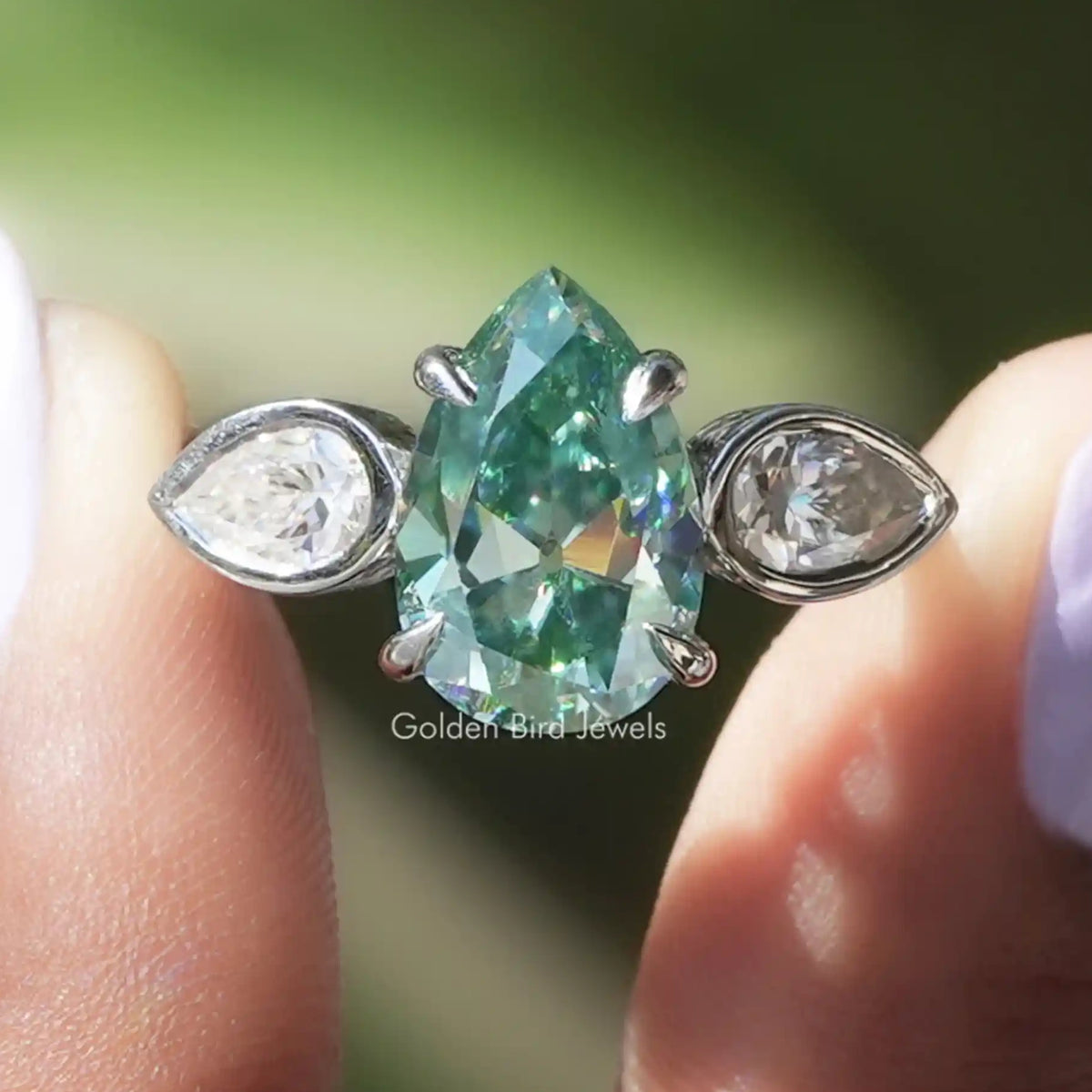 Three-stone ring with green pear-shaped center and two clear side stones, silver-tone.