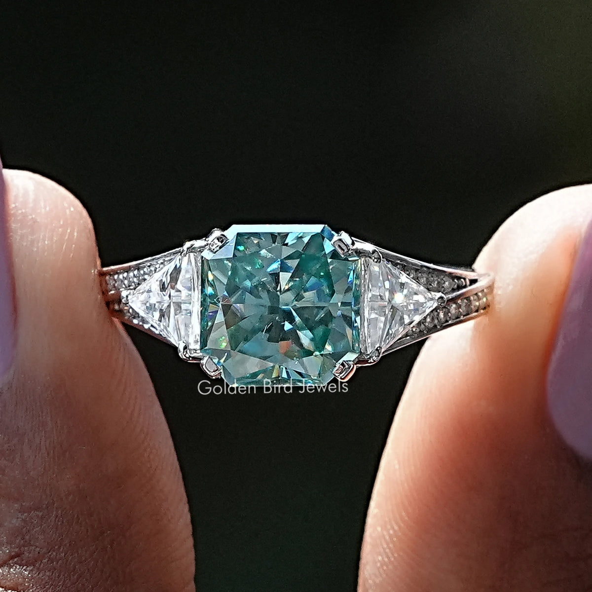 Moissanite accent stone ring with teal center and diamond-like side stones, prong set