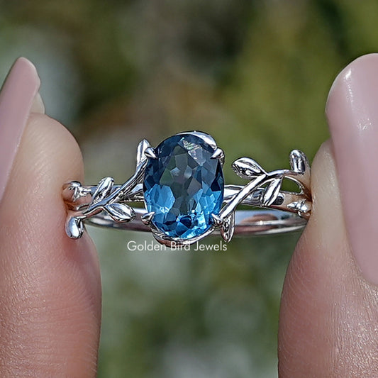 Oval blue gemstone engagement ring with silver prongs and leaf side details