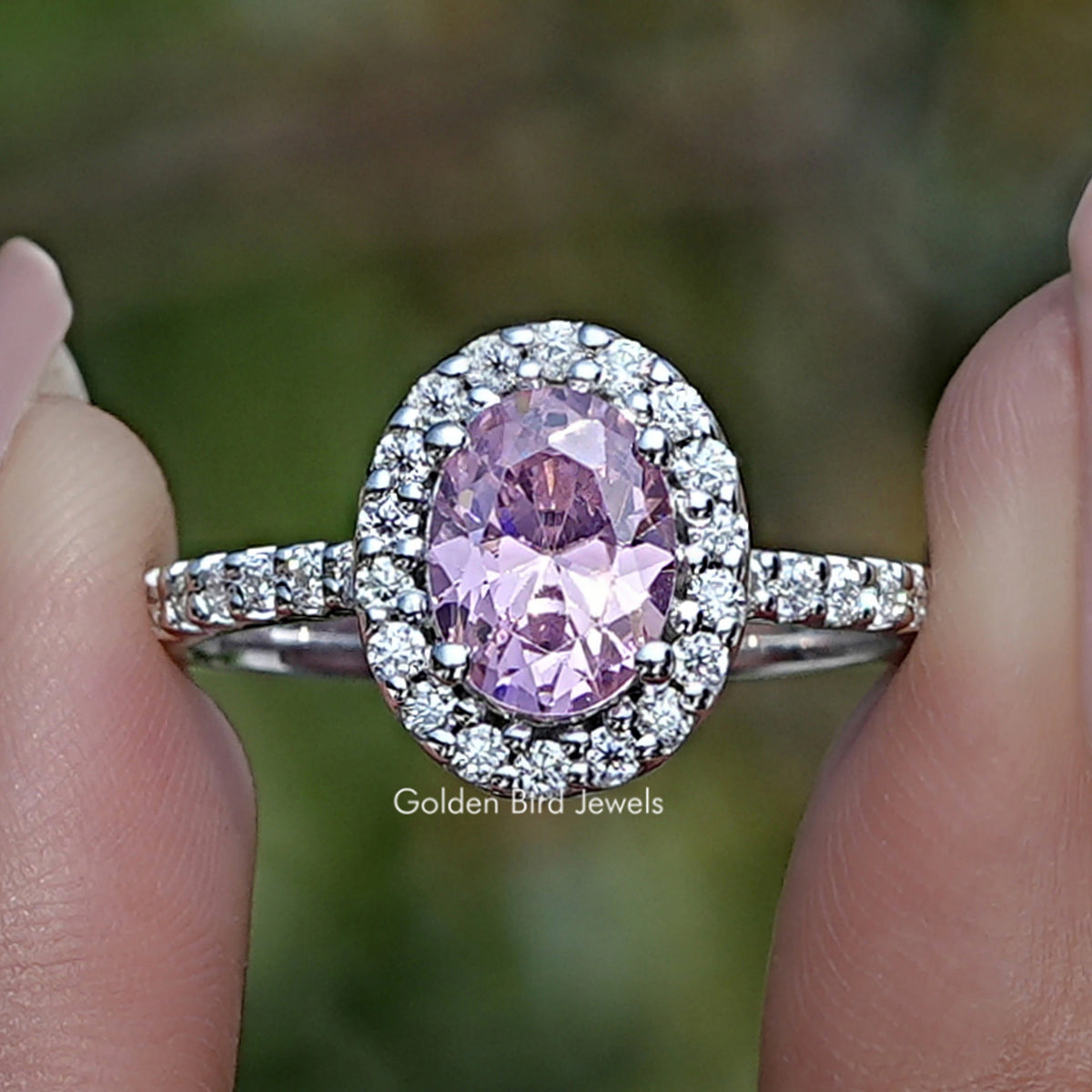 Oval pink gemstone halo ring with clear stone accents on a silver band